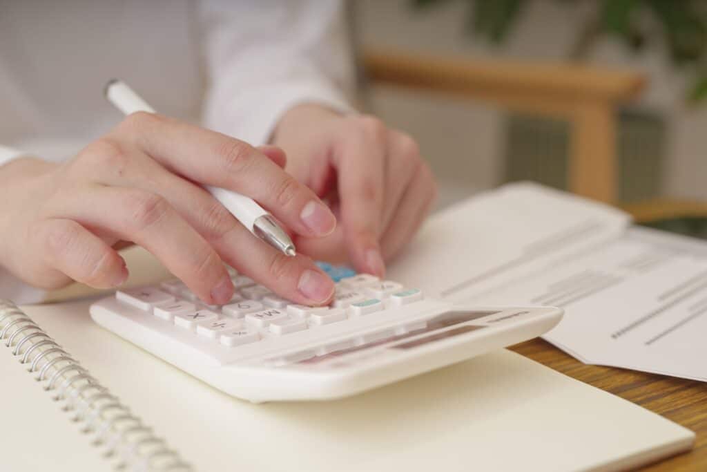 A person's hands using a calculator with a pen in the other hand, surrounded by a notebook and paperwork.